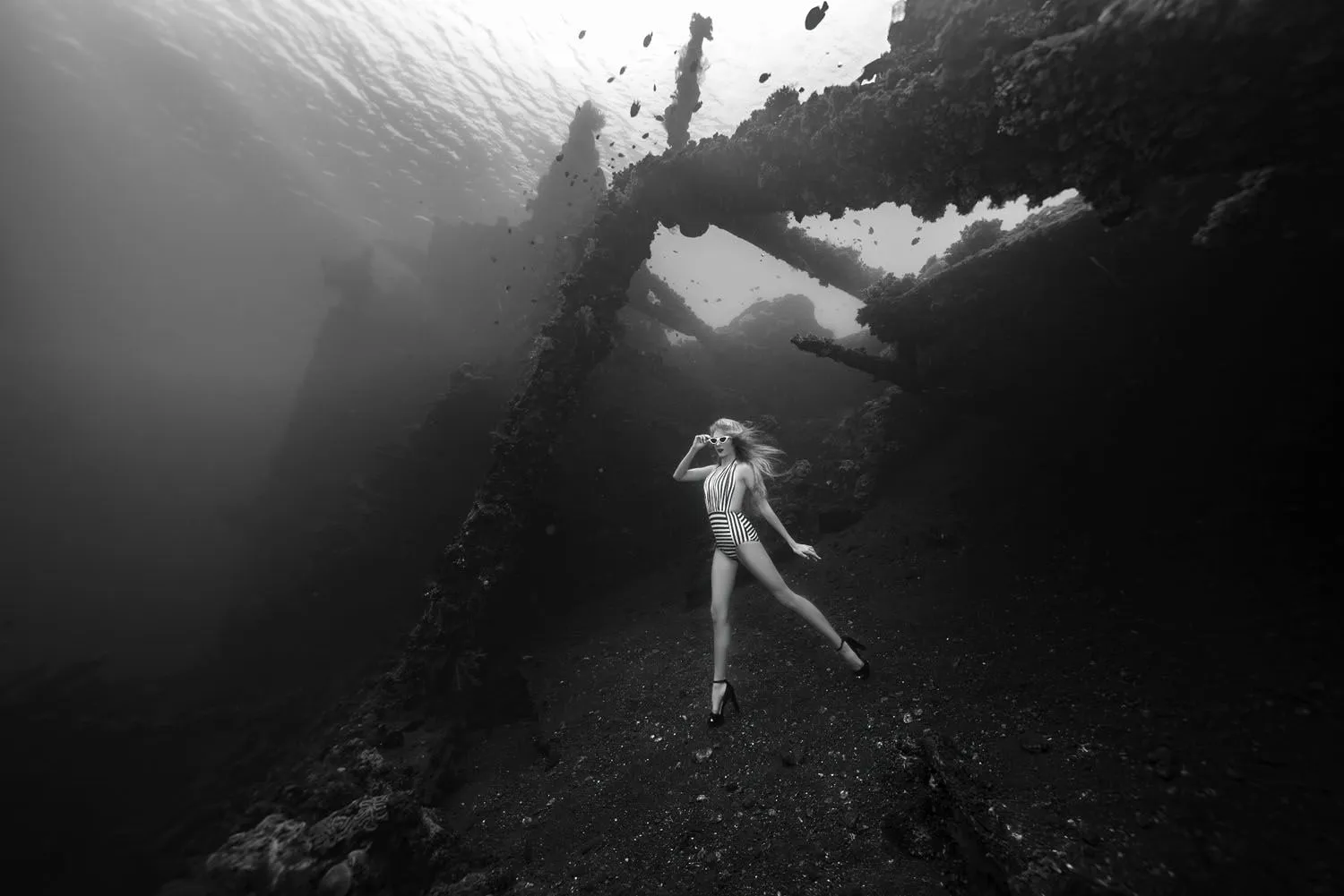 Black and white: a model in a striped swimsuit stands on the seabed beneath the beams of the Liberty wreck.