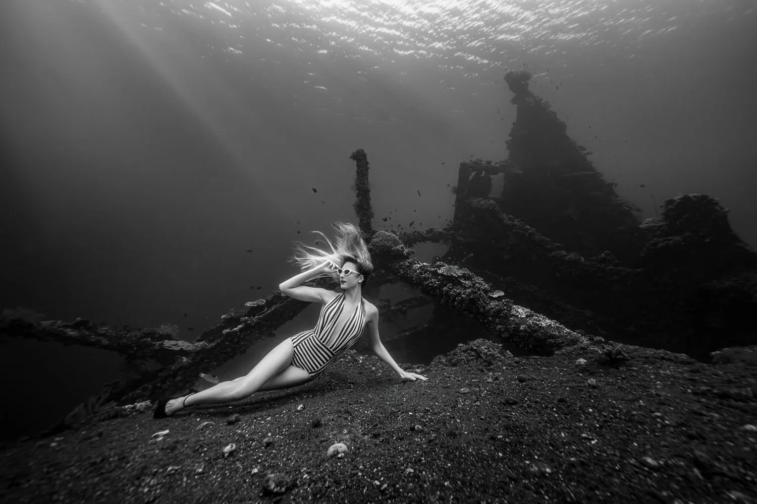A model in a striped swimsuit reclining against the wreck, one hand at her hair, beams of light behind her.