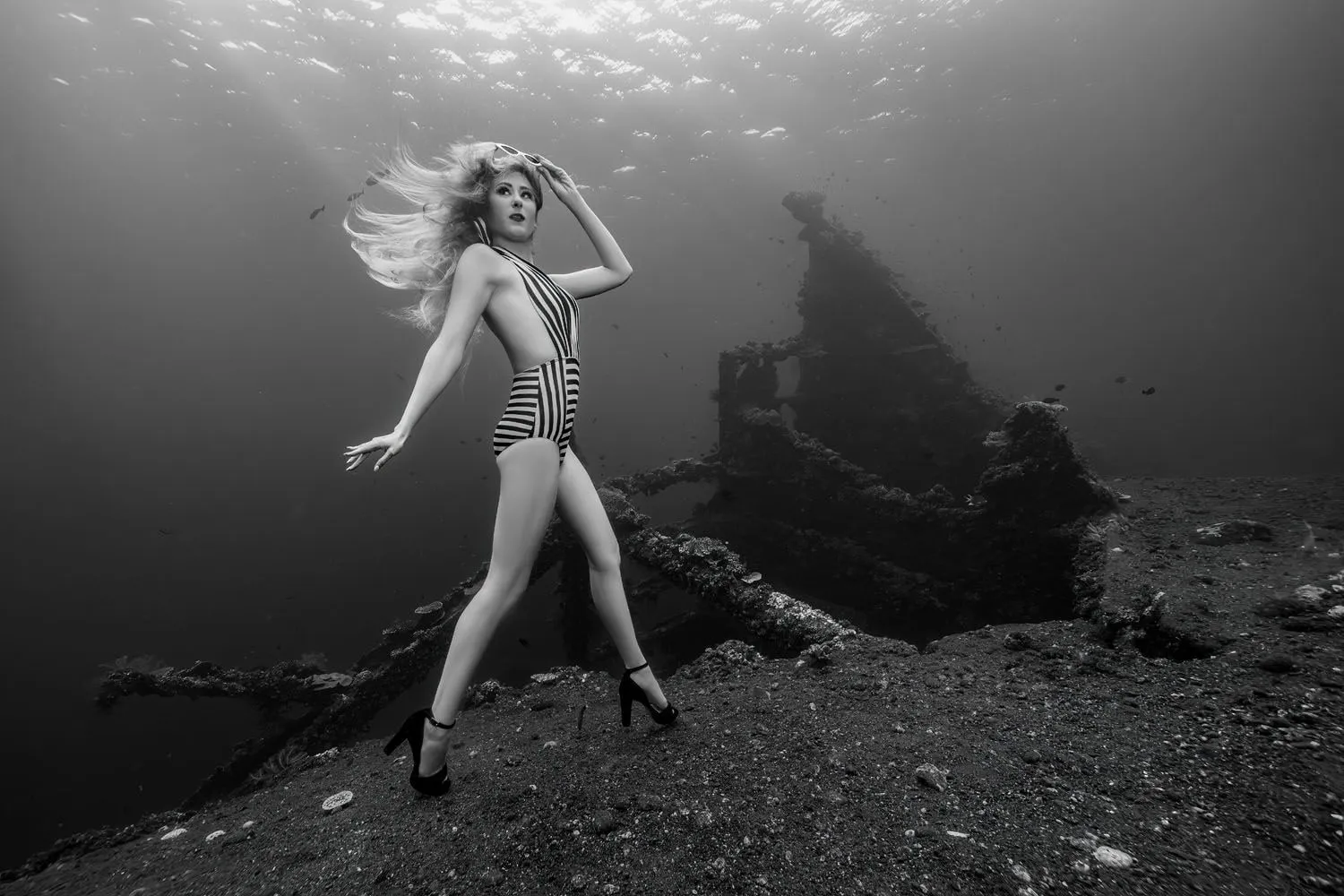 A model in a striped swimsuit and heels, hair lifting in the current, before the wreck of the Liberty.