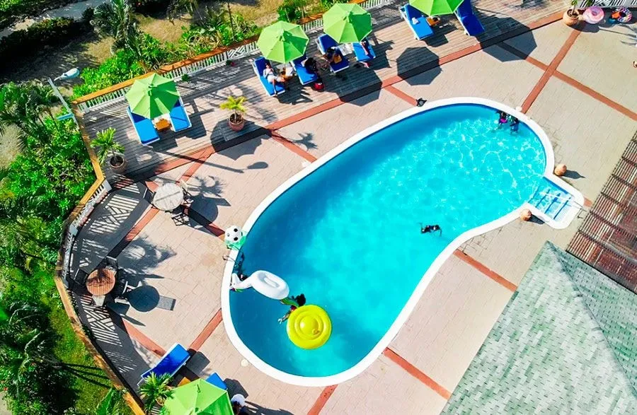 The resort pool from above, a kidney-shaped pool with loungers and green umbrellas on the terrace.