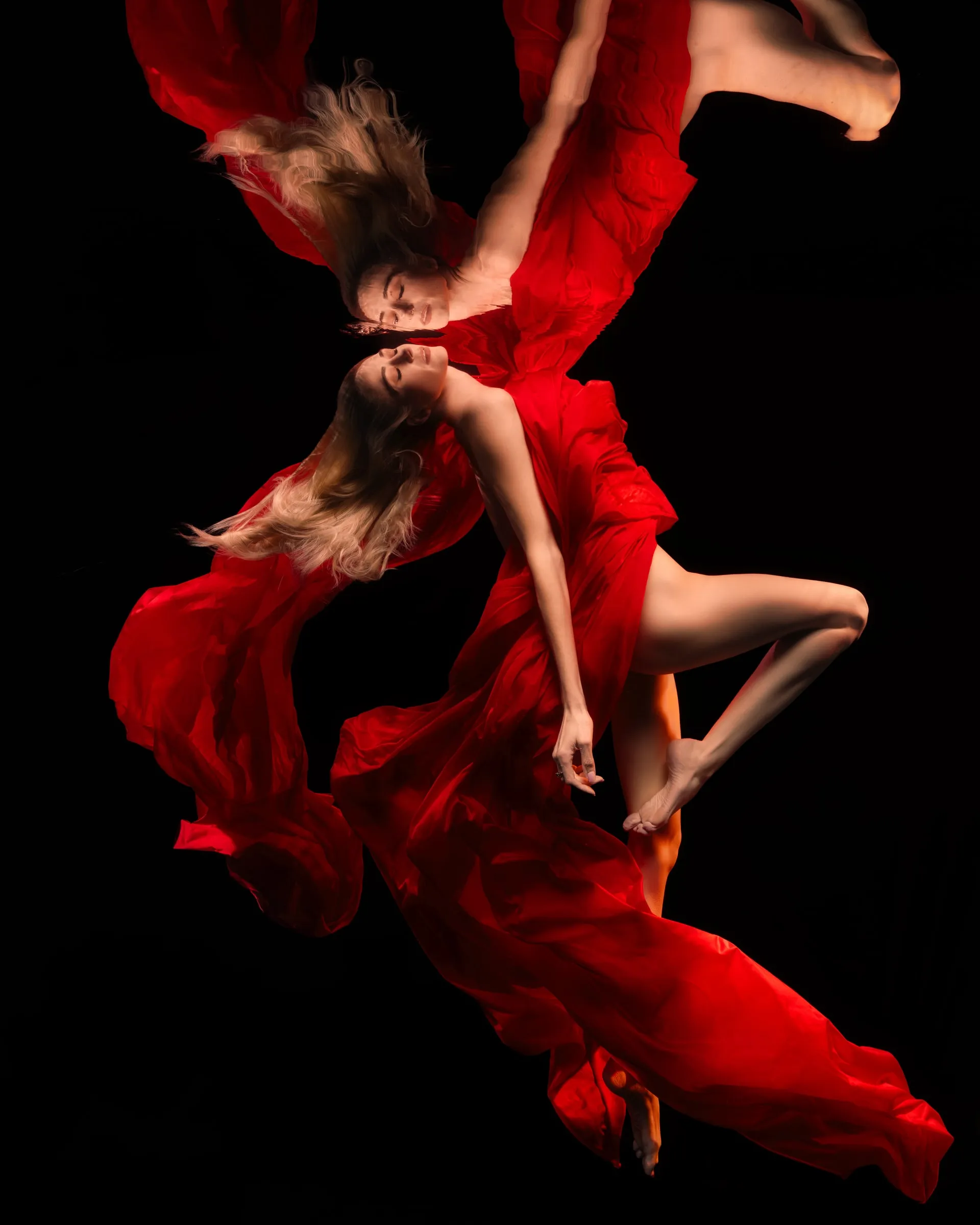 A performer wrapped in flowing red silk arches backwards just beneath the surface, her mirror image meeting her at the waterline.