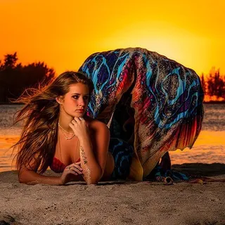 A woman lies on the sand at sunset, a blue and orange patterned fabric draped behind her, the sky a deep orange.