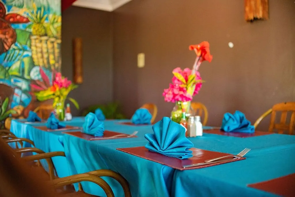 A restaurant table set with turquoise cloths and napkins and fresh flowers, a painted mural on the wall beyond.