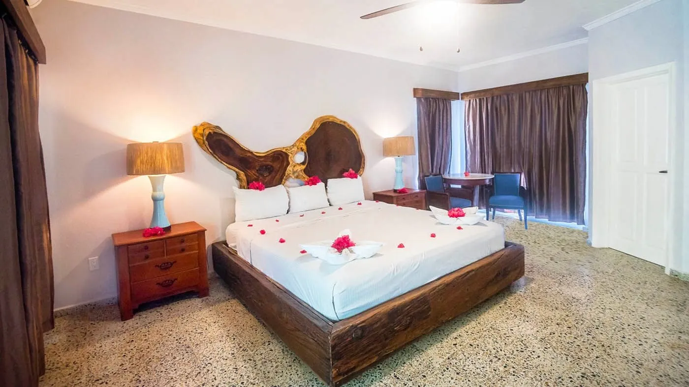 An Ocean View King room: a king bed on a timber frame with red petals and towel animals, ceiling fans overhead.