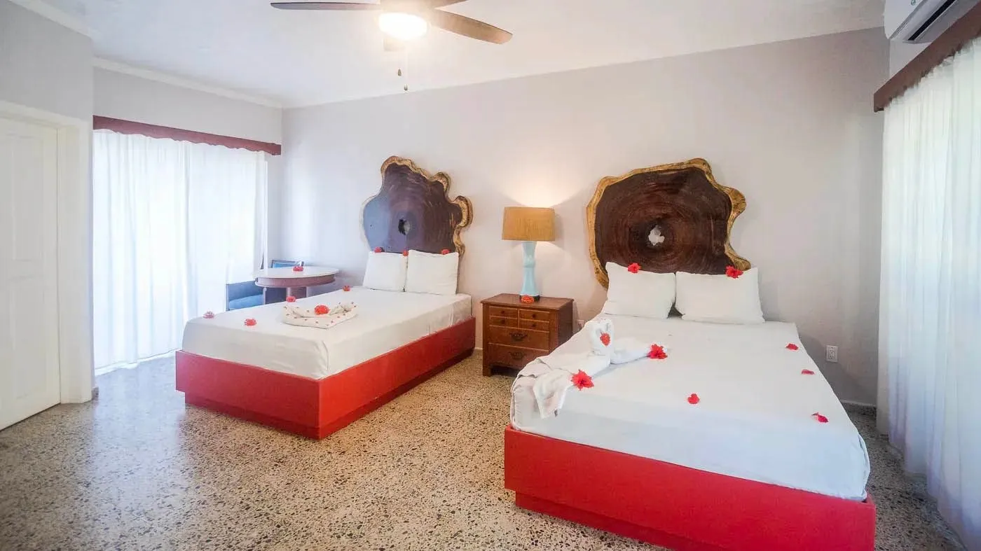 An Ocean View Double room: two beds with red bases and carved wooden headboards, white curtains at the windows.