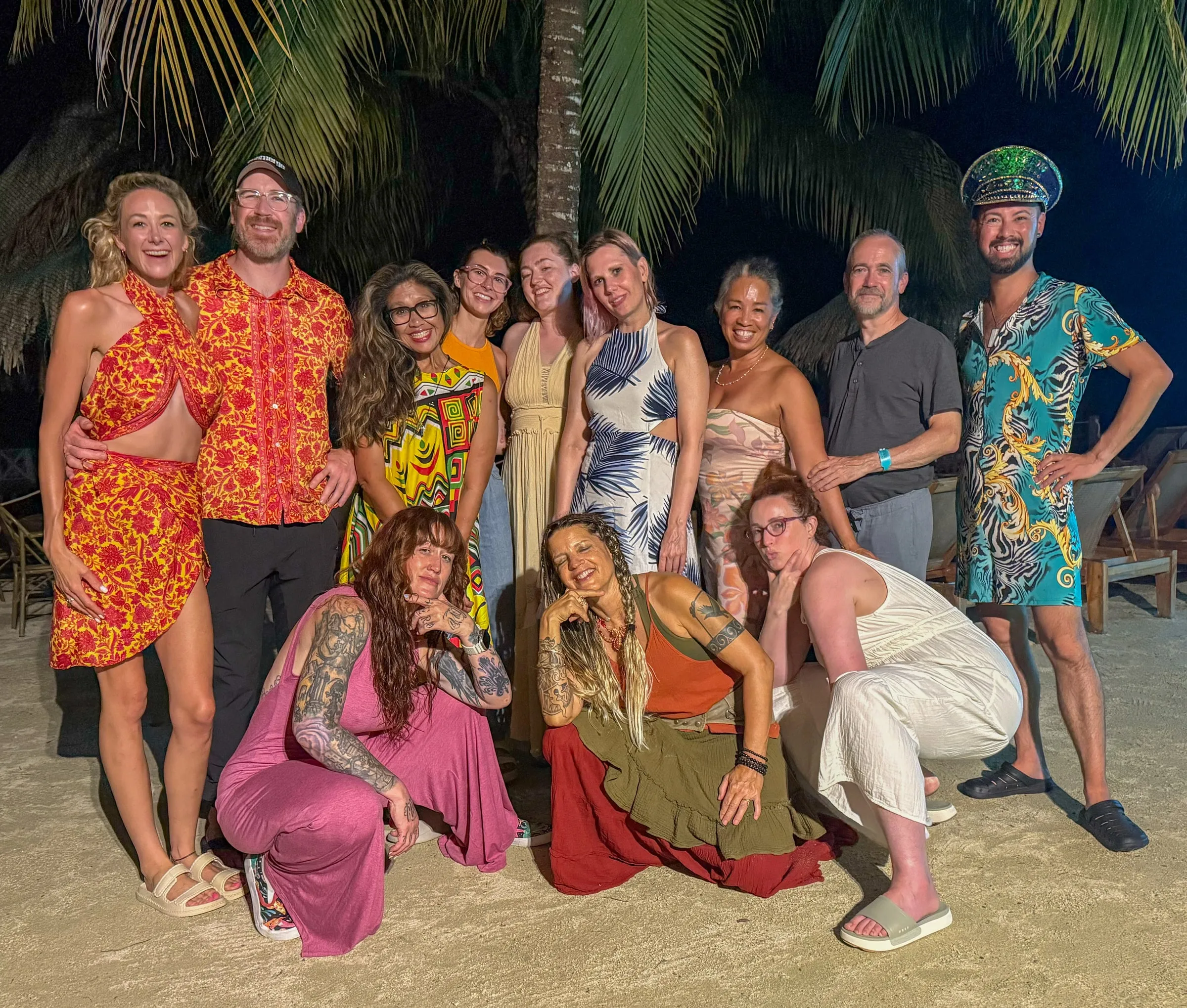 A night-time group photo on the beach, hosts and guests in colorful outfits under the palms.