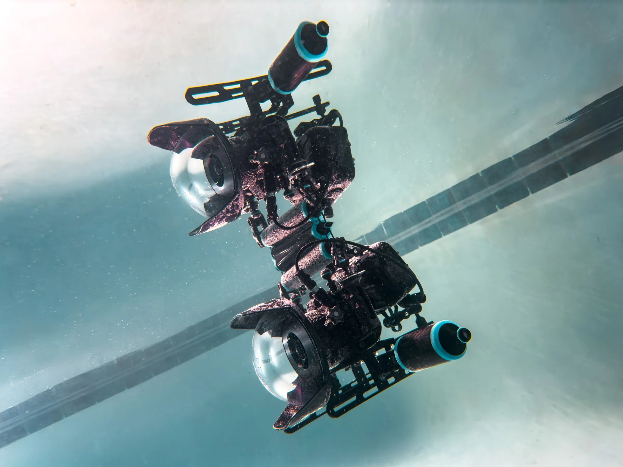 A camera rig with monitors and a dome port, seen from below against a pale pool floor.