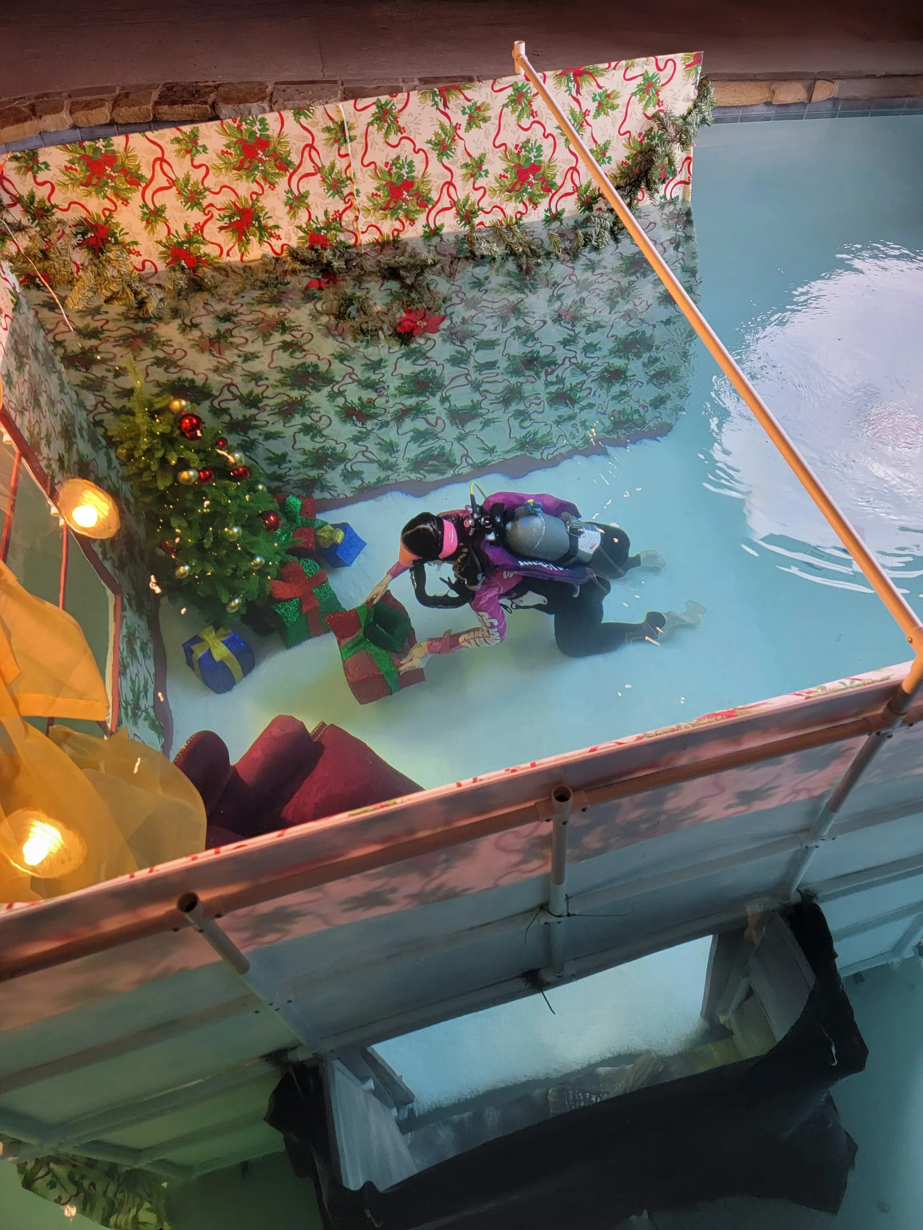 The studio pool seen from above, a diver in purple gear working inside a dressed holiday set with a lit tree.
