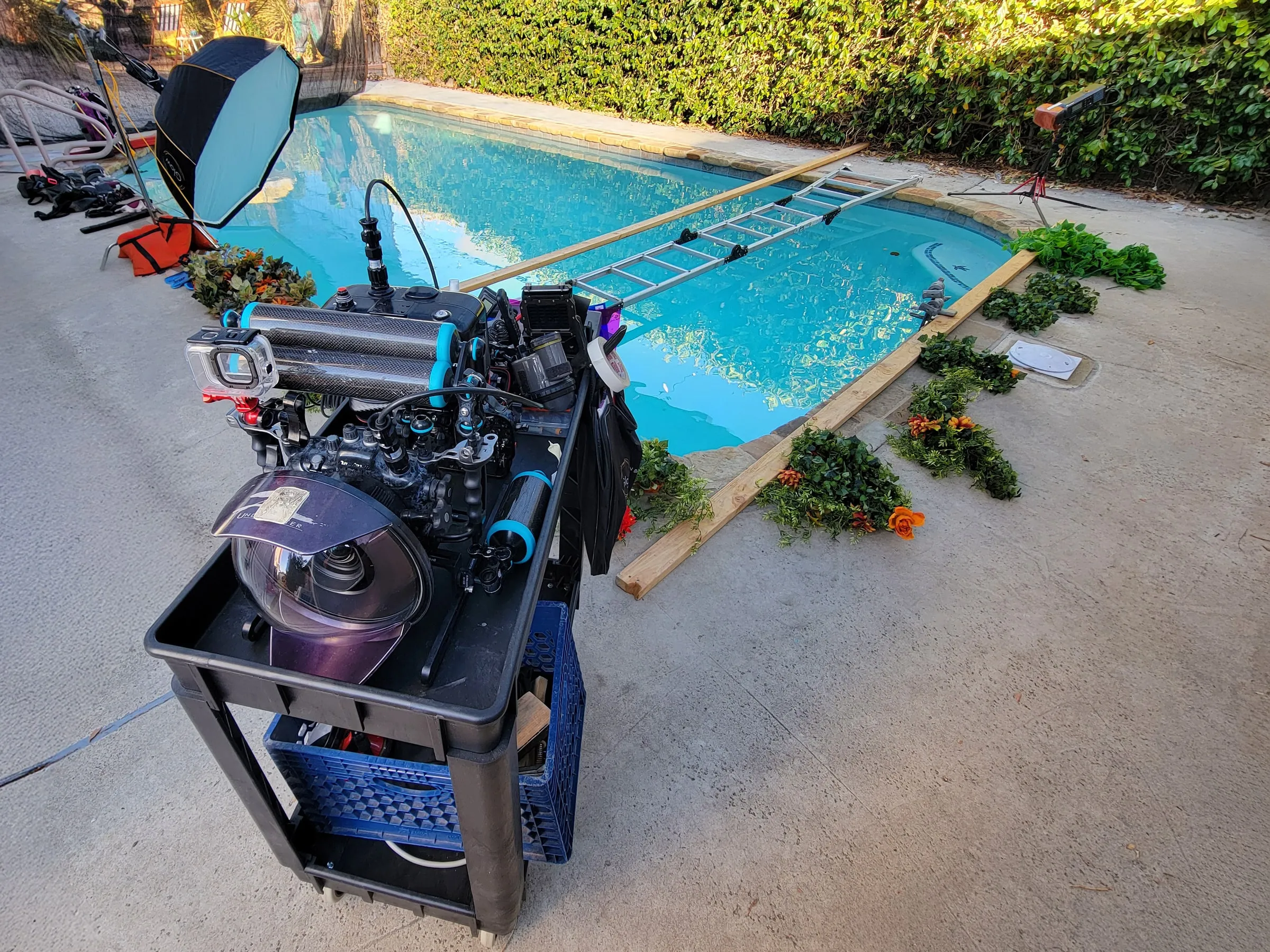 A camera cart loaded with a housed camera and dome port beside the studio pool, a softbox and a ladder bridge set up across the water.
