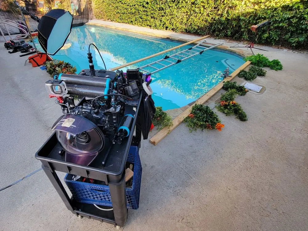 A cinema camera on a rig at the edge of the studio pool, beside a dressed set.